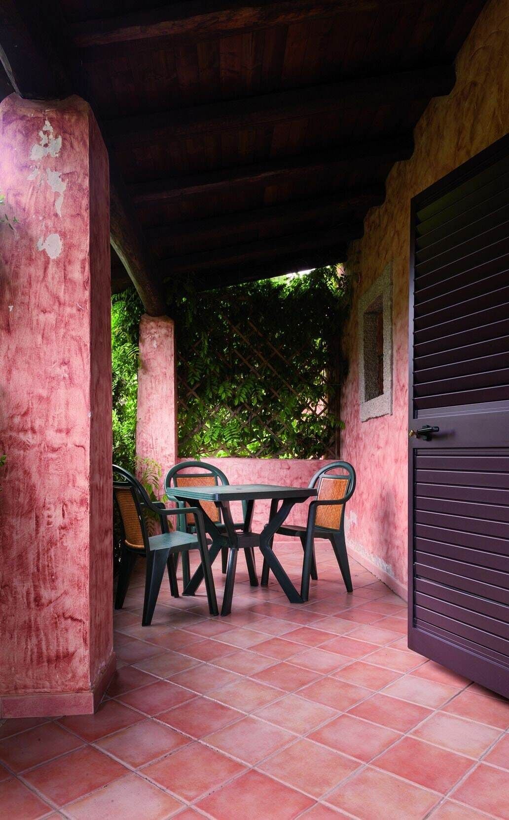 Un patio cubierto con mesa y sillas, piso de baldosas y una puerta.