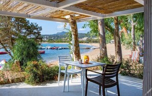 An outdoor patio with a table and chairs overlooking a beach and boats. - Centro Vacanza Isuledda (Arzachena)