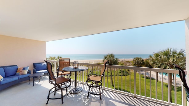Un balcon avec vue sur la plage, une table, deux chaises et un canapé.