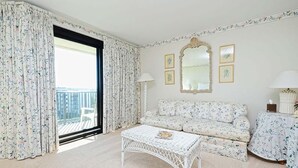 A room with a sofa, a white wicker coffee table, a round table with a floral tablecloth, a large mirror, and two framed pictures on the wall. - Coastal Oasis Inviting 3BR Condo with Resort Pool (Pawleys Island)