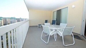 Ein Balkon mit weißer Brüstung, einem runden Tisch mit Stühlen und einer Schiebetür.