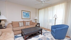 Ein Wohnzimmer mit einem beigen Sofa, einem blauen Sessel, einem Couchtisch und einem Deckenventilator.