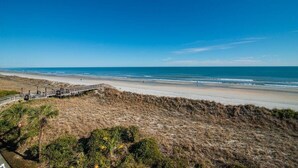Una playa con un paseo marítimo de madera, dunas arenosas y vegetación escasa.