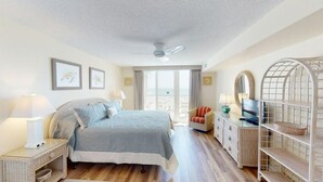 A bedroom with a bed, a chair, a TV, and a wicker side table.