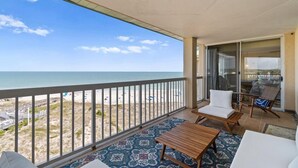 Un balcon avec vue sur la plage, une table, deux chaises et un canapé.