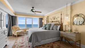 Une chambre à coucher comprenant un lit, une chaise, une commode et une fenêtre donnant sur l’océan.