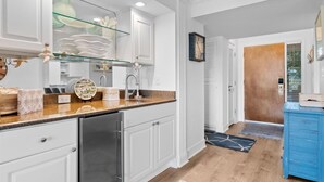 A modern kitchen with white cabinetry, a stainless steel refrigerator, and a glass shelf.