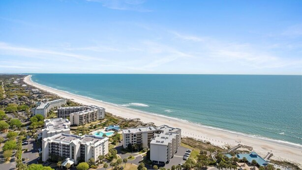 A coastal hotel with multiple buildings, a beach, and a clear sky.