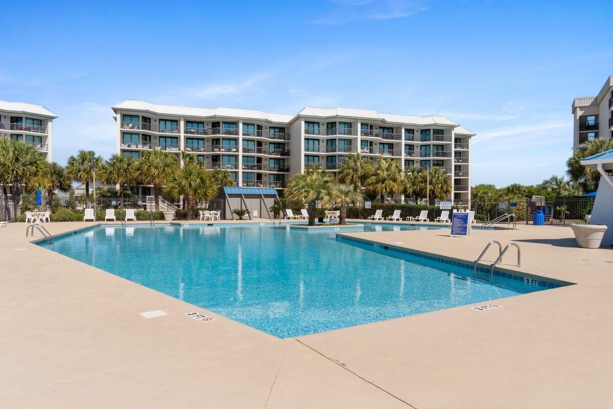 A rectangular swimming pool with clear blue water, surrounded by lounge chairs and palm trees.