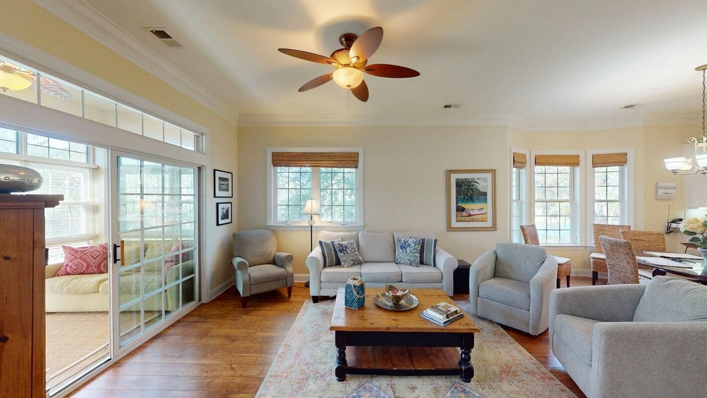 A spacious living room with a large ceiling fan, a wooden coffee table, and a view through a glass door.