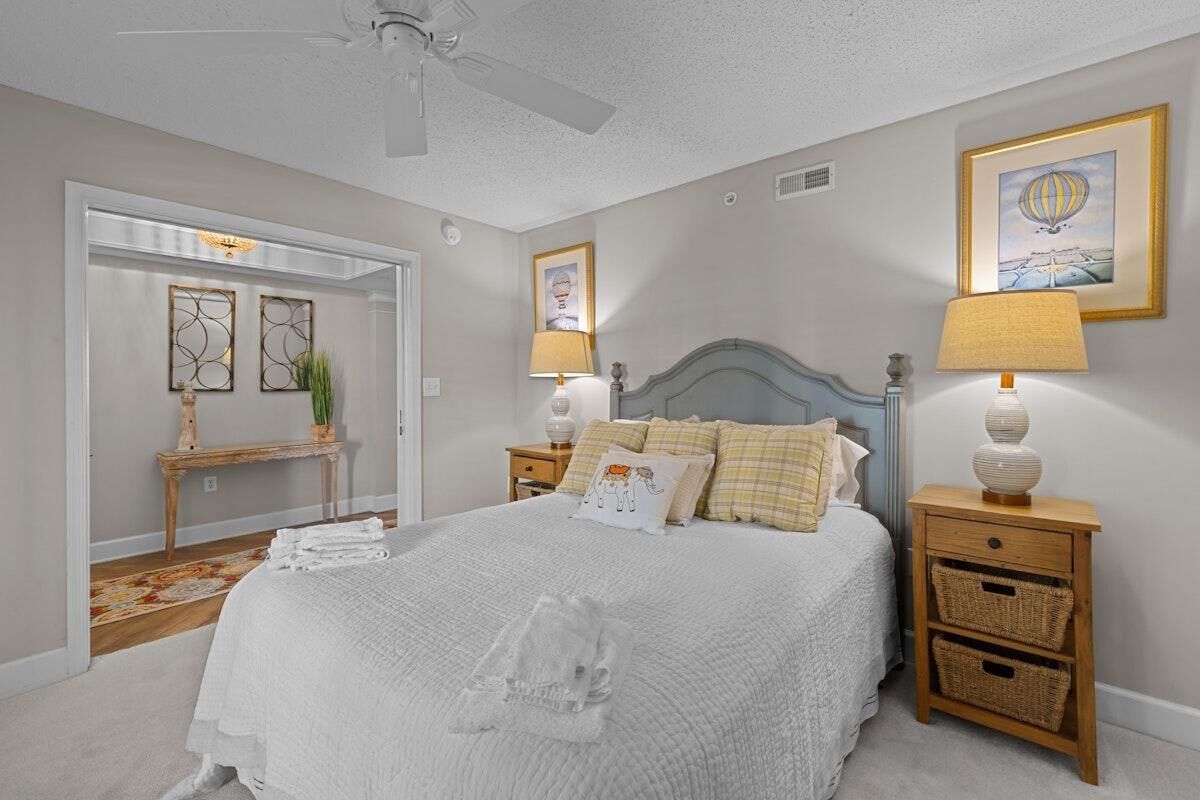 A bedroom with a bed, bedside tables, a nightstand, a ceiling fan, and a door leading to another room.