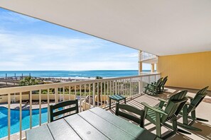 A balcony with a view of the ocean, a pool, and outdoor seating.
