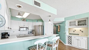 A kitchen with white cabinets, a central island with bar stools, and a microwave.