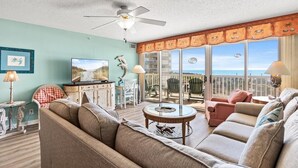 A living room with a sofa, chairs, a television, and a balcony with a view.