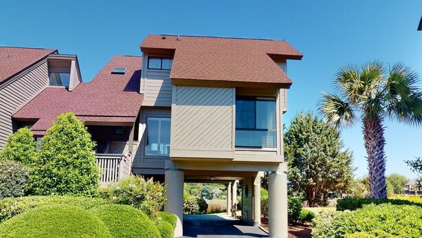 A multi-story residential building with a sloped roof, a covered entrance, and a landscaped garden with palm trees. - Lakeside Retreat Spacious 3BR 2BA Resort Amenities (Pawleys Island)