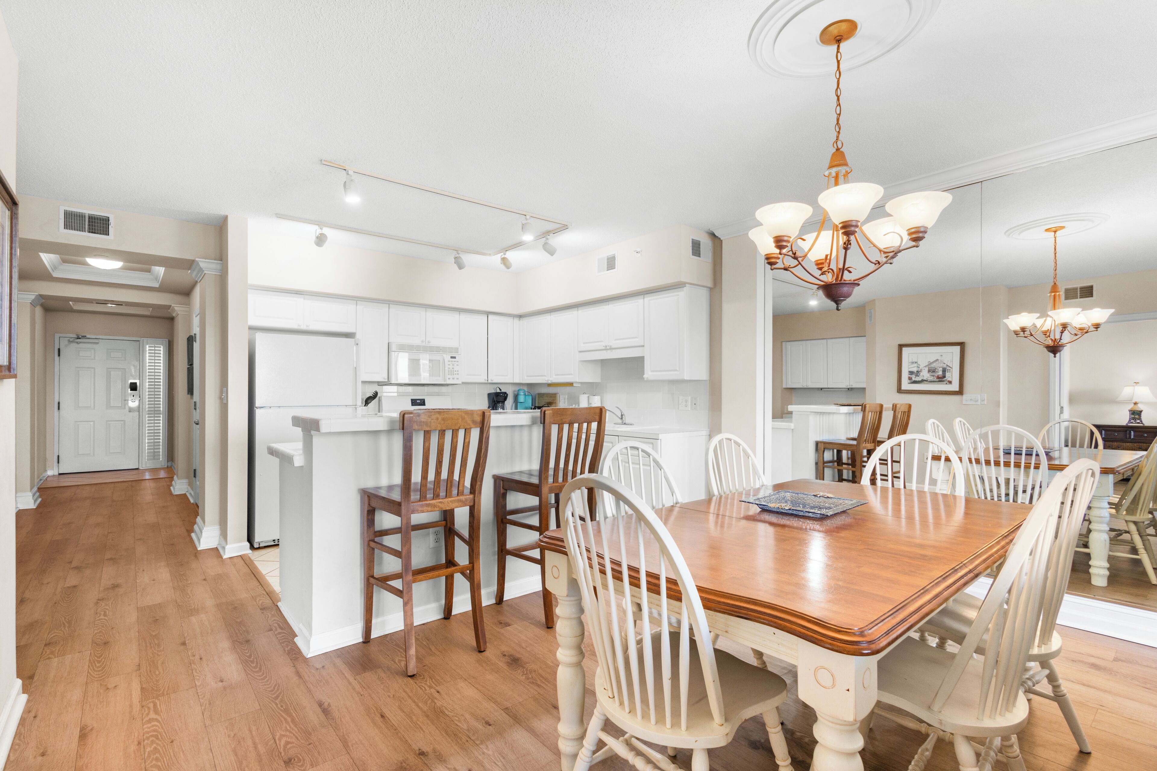 A spacious kitchen with white cabinets, a wooden dining table, and a chandelier.
