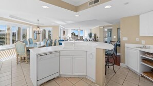 Een moderne keuken met een groot eiland, witte kasten en een eethoek met blauwe stoelen.
