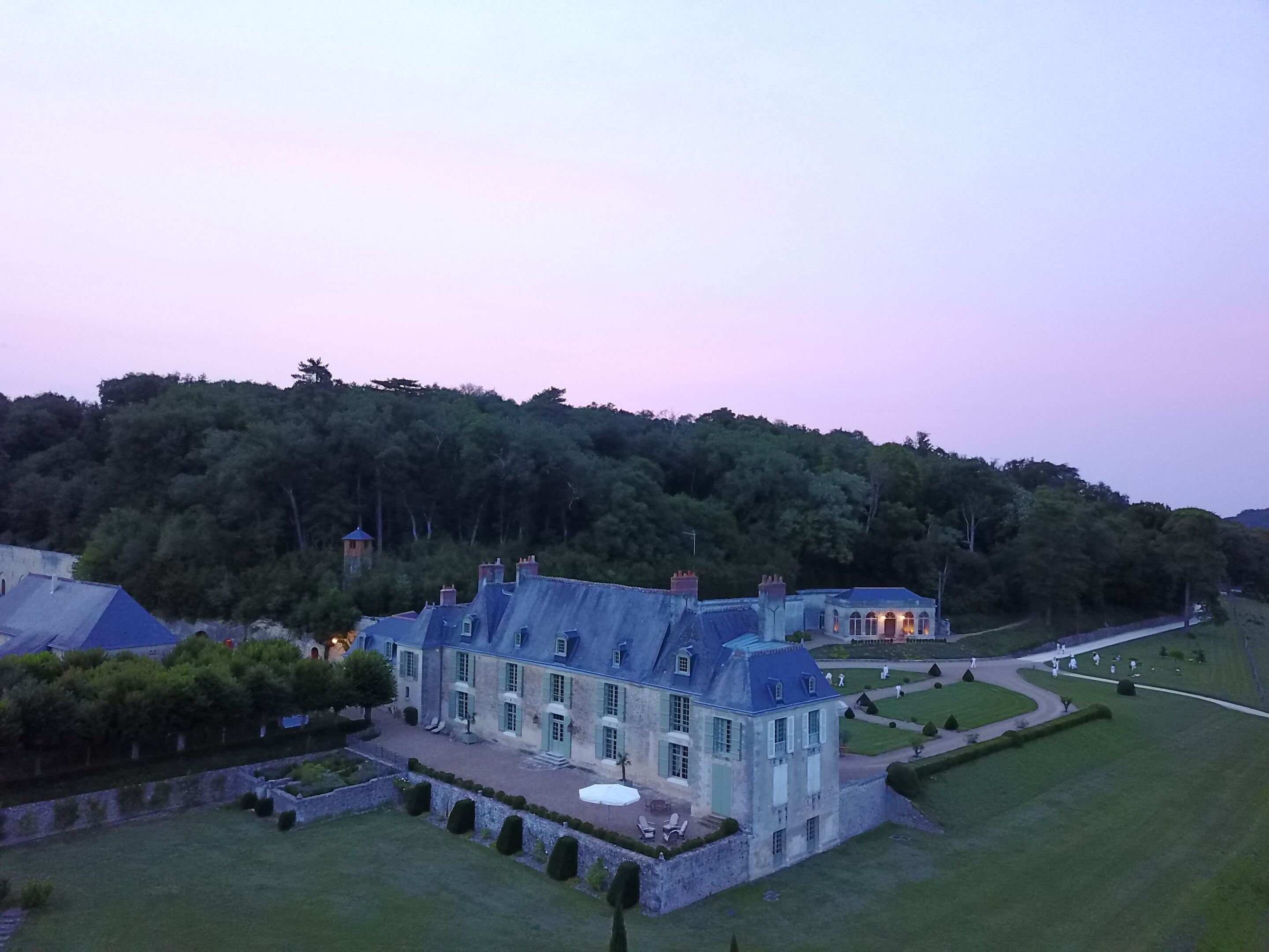 A large, historic building with a symmetrical facade, multiple chimneys, and a well-maintained lawn.