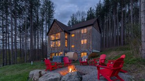 Een blokhut met een vuurkuil en rode Adirondack-stoelen, gelegen in een bos.