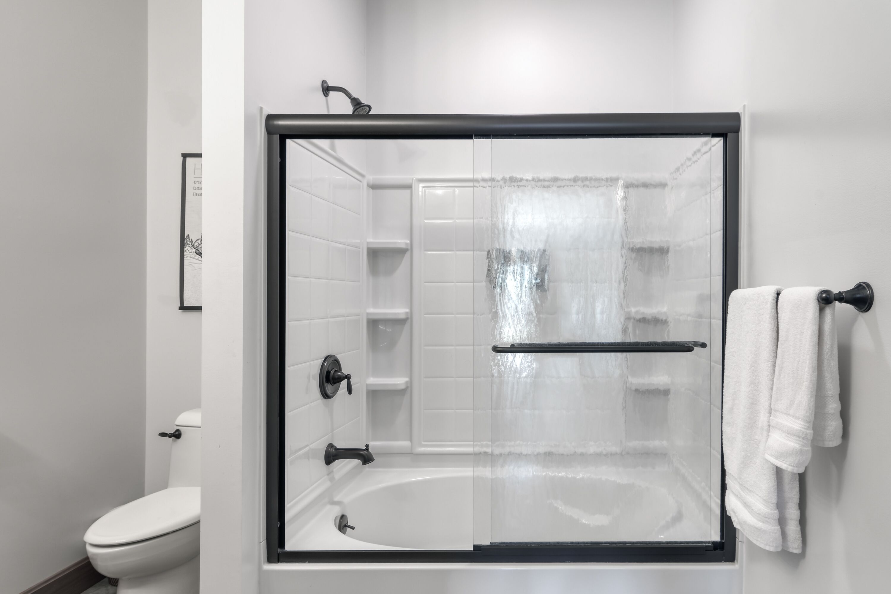 Un baño moderno con ducha envuelta en vidrio, inodoro y toallero.