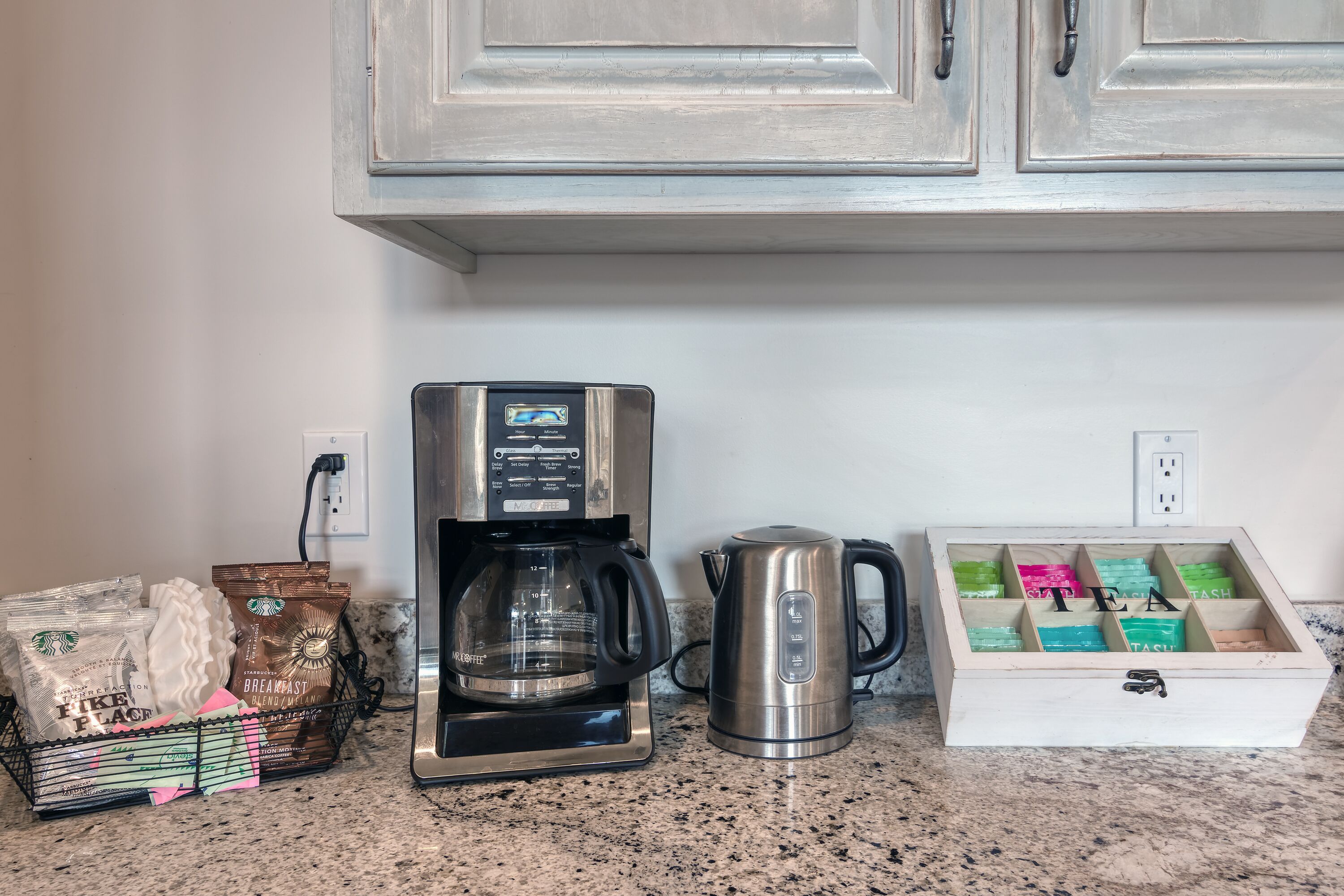 A kitchen counter with a coffee maker, a kettle, and a drawer organizer with tea boxes.