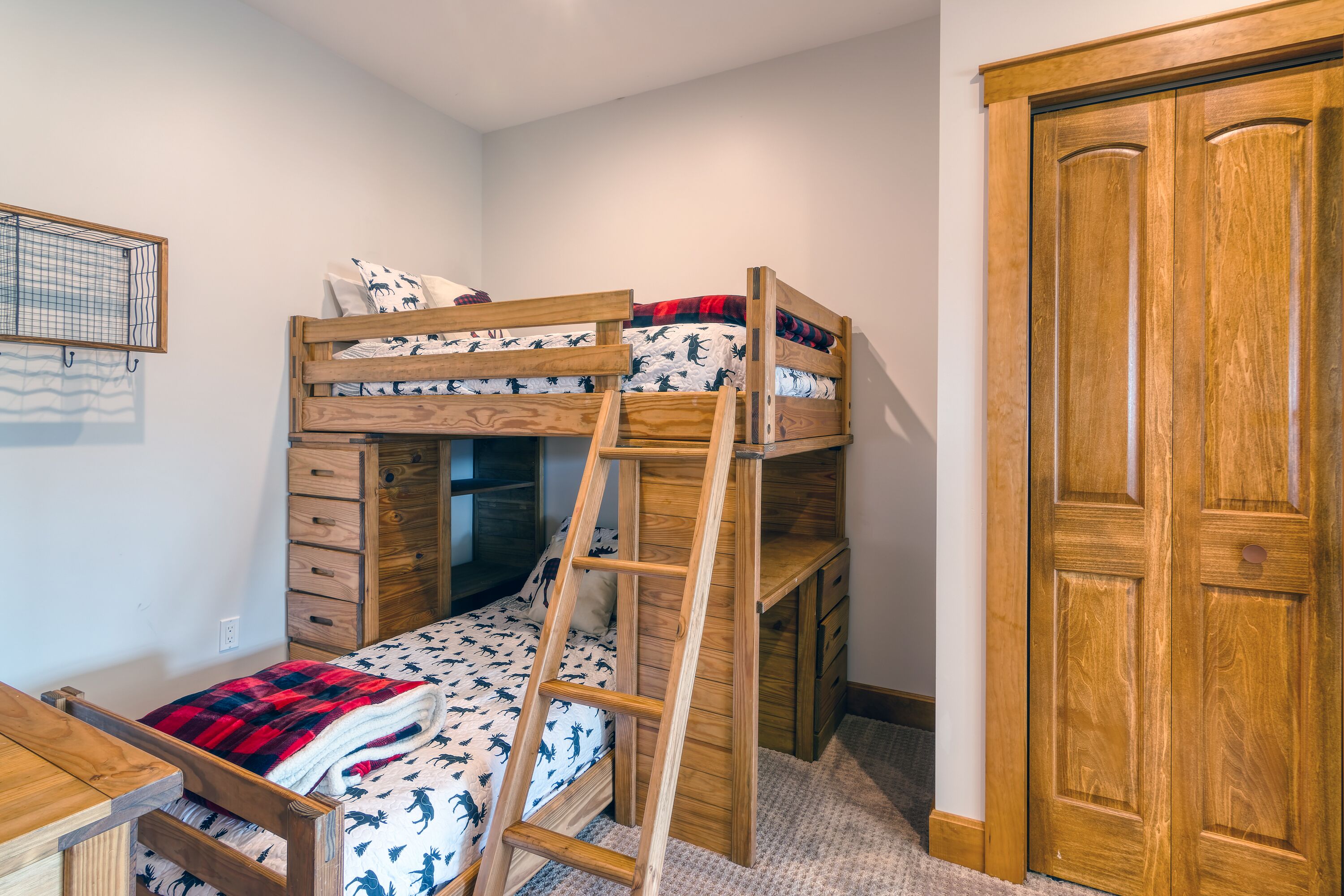 A bunk bed with a ladder, wooden drawers, and a wooden wardrobe.