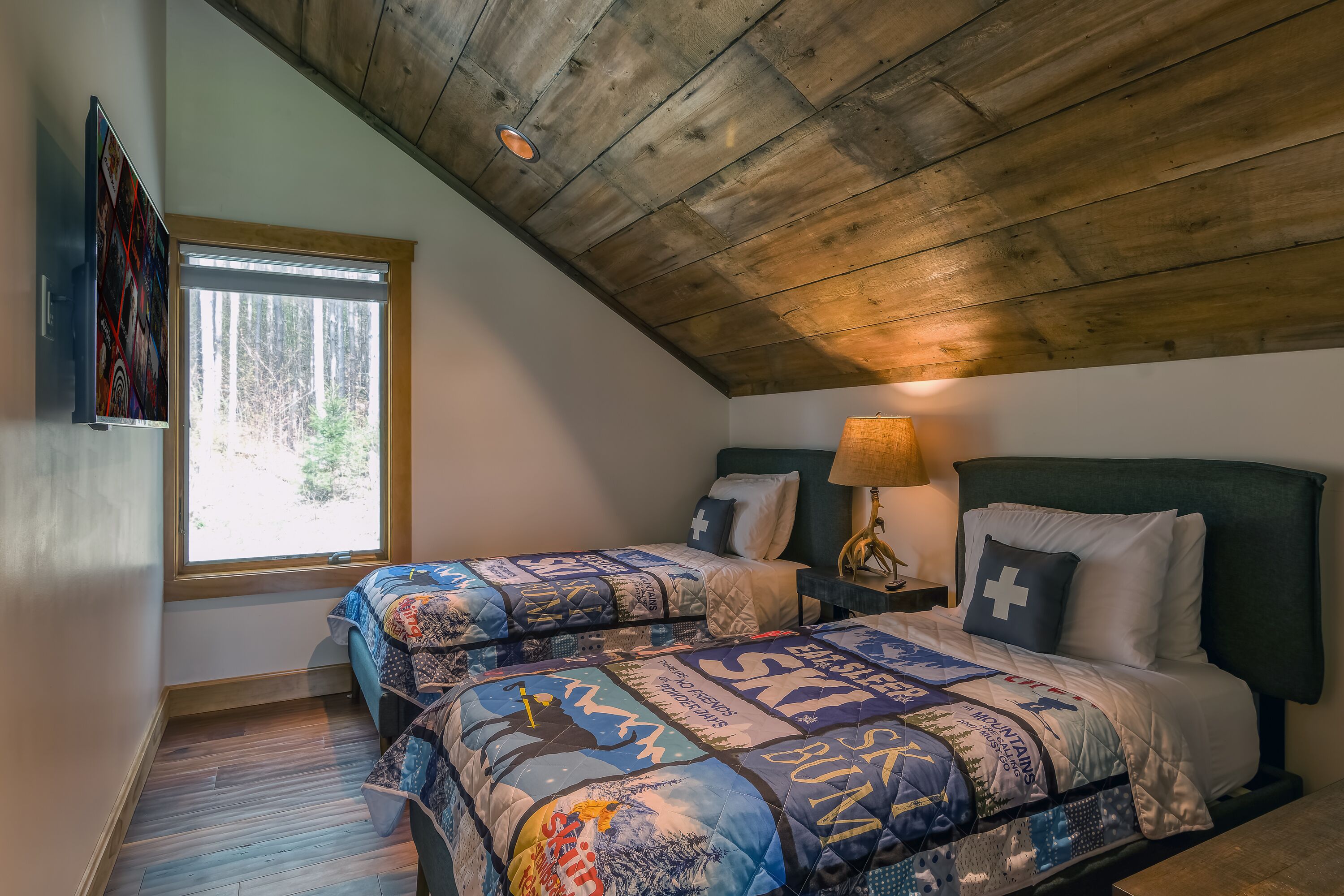 Ein Schlafzimmer mit zwei Betten, Holzboden, einem Fenster und einem an der Wand montierten Fernseher.