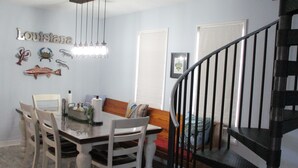 A dining area with a table, chairs, a chandelier, and wall decorations including the word "Louisiana". - Bayou Living (Barataria)