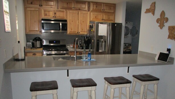 A kitchen with wooden cabinets, stainless steel appliances, and a bar stool area. - Bayou Living (Barataria)
