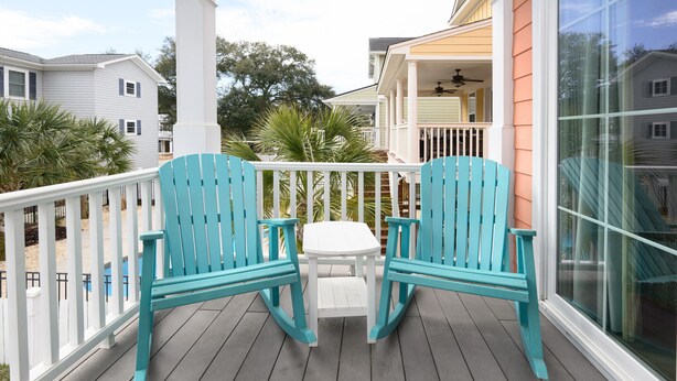A wooden deck with two turquoise Adirondack chairs and a small white table.
