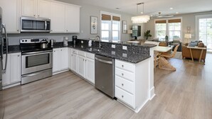A modern kitchen with white cabinets, a granite countertop, stainless steel appliances, and a dining area with a chandelier.