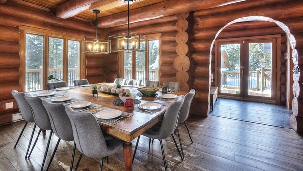A log cabin dining room with a large wooden table set for six, surrounded by grey upholstered chairs. - ☆TREMBLANT-Jaccuzi, lake access, pool table, 10 min ski⛷☀ (Lac Supérieur)
