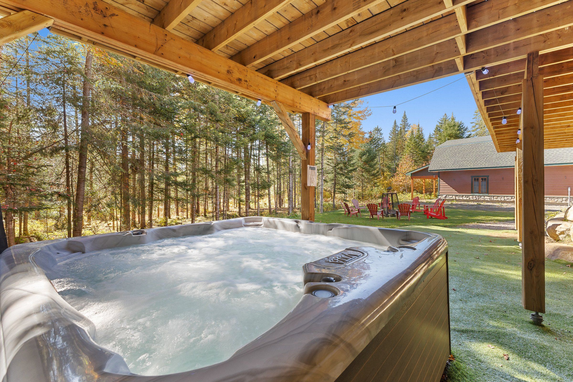 A hot tub under a wooden pergola with a forest backdrop.