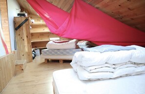 Une chambre confortable située sous les toits, avec un plancher en bois, un lit recouvert de draps blancs et un ciel de lit rouge.