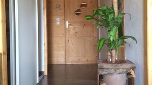 A wooden hallway with a door at the end, a potted plant, and a stack of firewood.