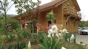 A wooden house with a balcony, surrounded by a garden with various flowers and plants.