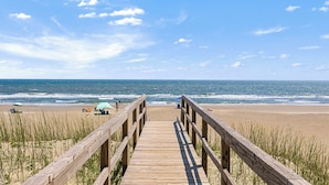 A wooden boardwalk leading to a beach with a clear view of the ocean.