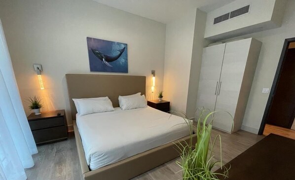Un dormitorio con cama, mesitas de noche, una mesita de noche con lámpara, un armario y una obra de arte colgada en la pared con una ballena.