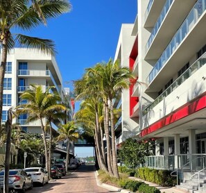 A modern hotel with a central walkway lined with palm trees, a red and white facade, and a clear blue sky.