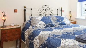 A bedroom with a bed, two bedside tables, a wall clock, and a window with a blue blind.