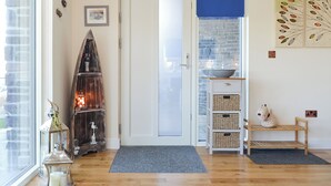 A room with a wooden floor, a white door, a blue window blind, wicker baskets, a small wooden bench, and a decorative lantern.