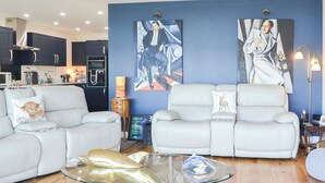 A modern living room with two white leather sofas, a glass coffee table, and artwork on the walls.