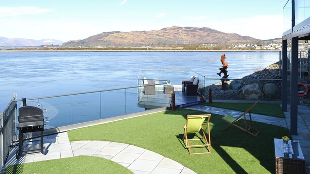 A patio with a grill, seating, and a view of a lake and mountains.