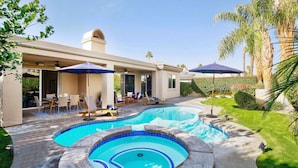 A swimming pool with a hot tub, outdoor seating, and a covered patio area.