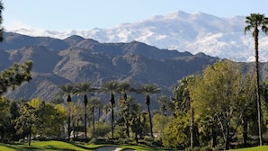 A golf course with a mountainous backdrop, palm trees, and a clear sky.