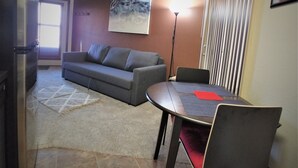 Ein Wohnzimmer mit einer Couch, einem Esstisch mit Stühlen, einem Kühlschrank und einem Bild an der Wand.