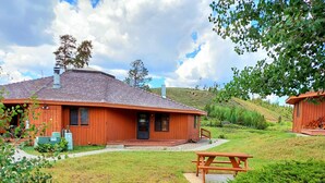Eine Holz-Blockhütte mit Veranda, Picknicktisch und Rasenfläche.