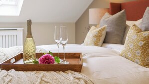 Une chambre à coucher avec un lit, des oreillers, une table de chevet sur laquelle se trouvent une bouteille et des verres, et une fenêtre.