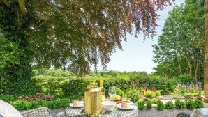 Un espace de restauration en plein air, avec des meubles en osier, un vase décoratif et une table dressée avec de la nourriture et des boissons.