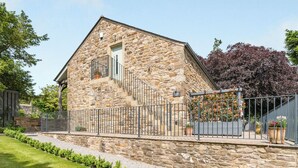 Un bâtiment en pierre doté d’un escalier, d’un petit balcon et d’un jardin entouré d’une clôture.